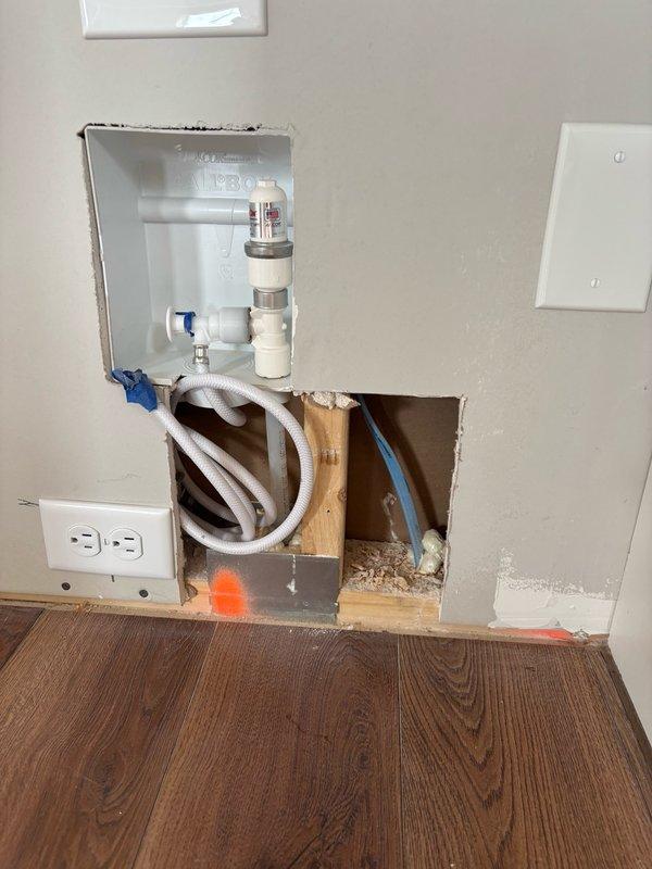 Cut out drywall section at floor level to create recessed access for refrigerator water line installation. Repositioned ice maker valve approximately 6 inches to allow flexible tubing to sit flush within wall cavity, enabling refrigerator to fit properly against wall. Confirmed placement with homeowner before and after modification, verified all connections were secure, and left system in service with water supply operational.