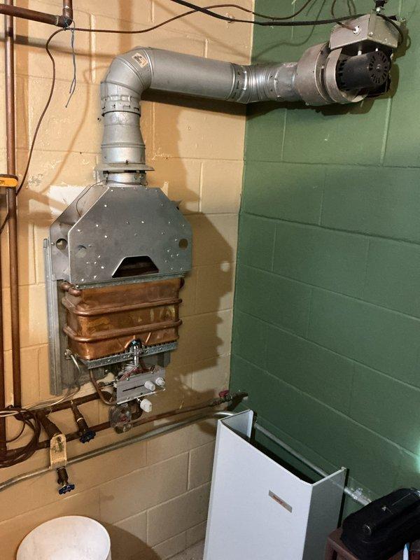 Responded to service call for tankless water heater with pilot light that would not remain lit. Upon inspection, determined that the pilot ignition system was weak and the unit was struggling to maintain proper operation. Documented existing installation with photos showing wall-mounted tankless unit with copper heat exchanger, venting system, and associated plumbing connections. Evaluated system performance and determined that repair of the failing ignition components would not be cost-effective given the age and condition of the unit. Provided estimate for replacement with conventional tank-style water heater as a more reliable long-term solution.