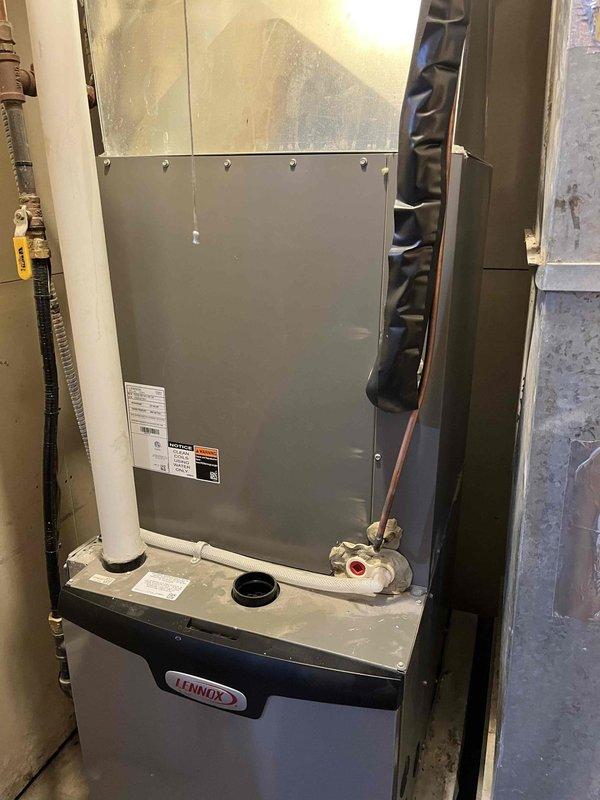 Replaced the evaporator coil assembly with integrated drain pan on a 2-year-old Lennox vertical furnace unit under full warranty due to drain pan leakage. Disconnected and removed the failed evaporator coil, installed the new replacement unit, evacuated the refrigerant system to proper vacuum specifications, and recharged the system to manufacturer specifications. Verified proper system operation with a 23-degree temperature split across the coil and confirmed the drain pan is functioning correctly without leakage.