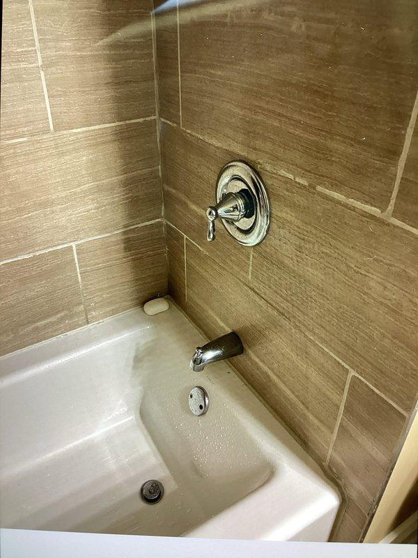 Responded to multiple shower-related issues including a slow leak from the master shower, low water pressure in a secondary shower, and a malfunctioning shower valve. Upon inspection, determined the shower cartridge was defective and the entire valve assembly was not functioning properly. Replaced the faulty shower cartridge and valve system. Addressed deteriorating tile grout in the shower area that was contributing to water leakage. Additionally, installed a handheld shower head unit in the basement shower as requested. Documented existing plumbing infrastructure including water heater and supply lines. All fixtures tested and confirmed operational upon completion.