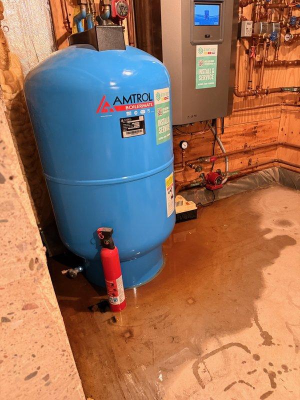 Responded to water leak complaint at residential property. Upon inspection, identified failed condensation pump with broken hose adaptor as source of water accumulation on basement floor. Water pooling was not originating from the Amtrol Boilermate indirect water heater or its pressure relief valve as initially suspected. Documented conditions with photographs showing water staining on concrete floor around equipment. Coordinated with HVAC contractor for condensation pump replacement and repair of drainage system. Equipment in utility room includes indirect water heater system with associated controls and plumbing connections.
