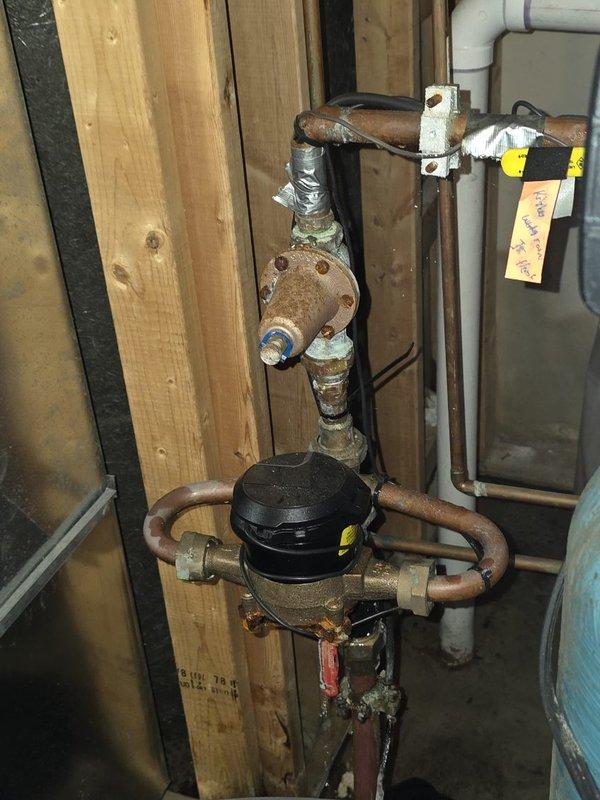Responded to water leak near the main water meter and shut-off valve assembly. Upon inspection, identified multiple leak sources including a failed compression seal at a pipe coupling connection and a pinhole leak in a secondary fitting body. The main water shut-off valve exhibited significant cracking and corrosion, rendering it unsafe for continued operation. Replaced the compromised main shut-off valve with new assembly to restore proper water control and prevent future failures. Repaired leaking compression fittings and addressed pinhole leak in the piping near the water meter and softener connection point. All copper piping, brass fittings, and valve components showed extensive oxidation and corrosion consistent with age and moisture exposure. Tested all connections for proper seal integrity and verified full system functionality upon completion.