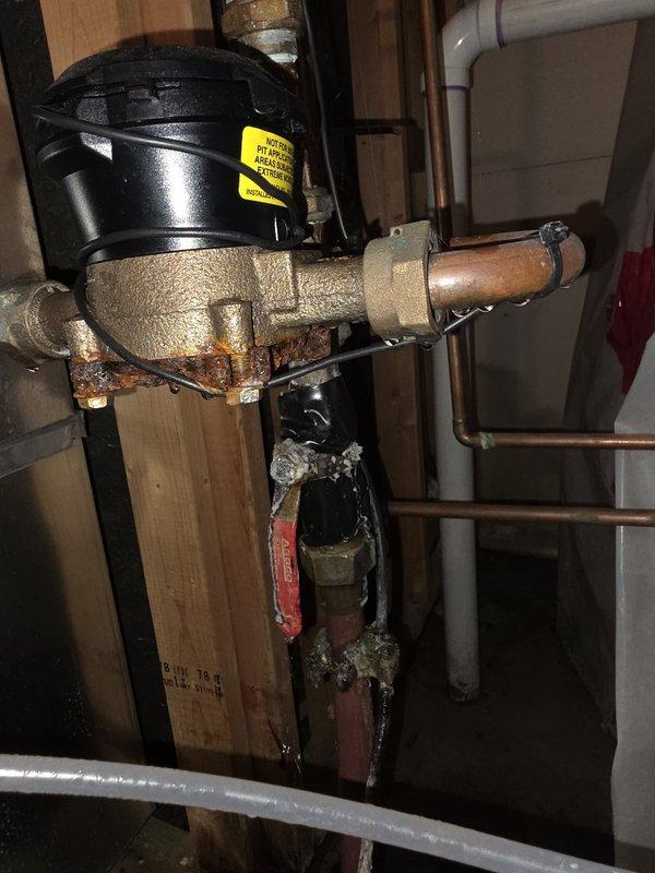 Responded to water leak near the main water meter and shut-off valve assembly. Upon inspection, identified multiple leak sources including a failed compression seal at a pipe coupling connection and a pinhole leak in a secondary fitting body. The main water shut-off valve exhibited significant cracking and corrosion, rendering it unsafe for continued operation. Replaced the compromised main shut-off valve with new assembly to restore proper water control and prevent future failures. Repaired leaking compression fittings and addressed pinhole leak in the piping near the water meter and softener connection point. All copper piping, brass fittings, and valve components showed extensive oxidation and corrosion consistent with age and moisture exposure. Tested all connections for proper seal integrity and verified full system functionality upon completion.