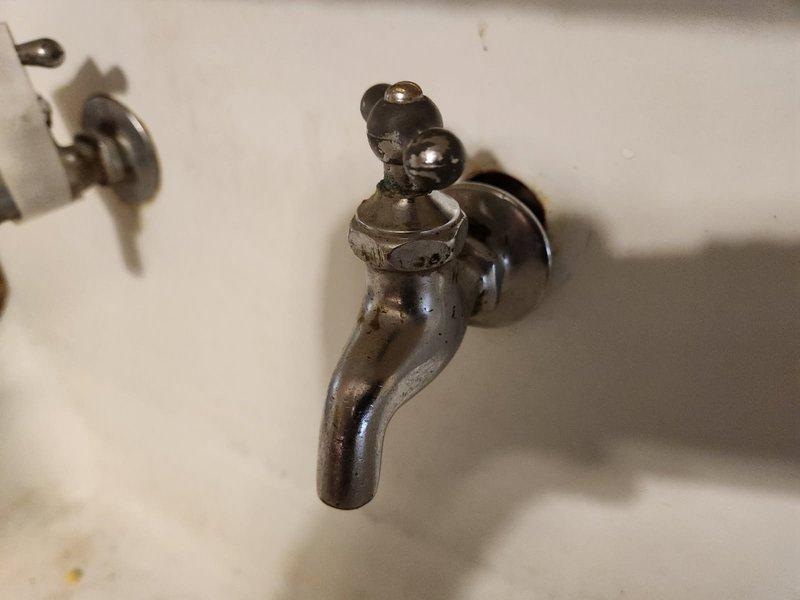 Responded to kitchen sink water leak caused by deteriorated faucet fixture. Inspected old farm-style ceramic sink with wall-mounted faucet showing significant corrosion, tarnishing, and finish deterioration. Documented existing conditions with photographs showing extensive oxidation and worn metal surfaces on single-handle fixture. Assessed mounting configuration and determined replacement necessary due to age and condition of existing hardware. Prepared parts order form to provide pricing options for new faucet with portable dishwasher hookup capability compatible with vintage sink mounting requirements.