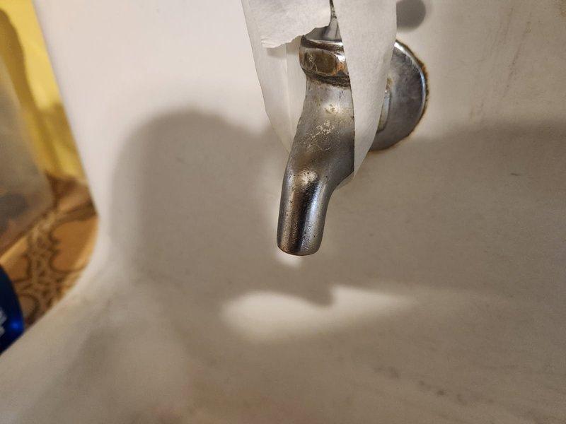 Responded to kitchen sink water leak caused by deteriorated faucet fixture. Inspected old farm-style ceramic sink with wall-mounted faucet showing significant corrosion, tarnishing, and finish deterioration. Documented existing conditions with photographs showing extensive oxidation and worn metal surfaces on single-handle fixture. Assessed mounting configuration and determined replacement necessary due to age and condition of existing hardware. Prepared parts order form to provide pricing options for new faucet with portable dishwasher hookup capability compatible with vintage sink mounting requirements.