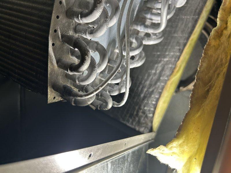 Responded to repeat no-cool complaint with system freezing and water accumulation at furnace. Upon arrival, verified coils were clean and air filter was new. Placed system in charge mode and confirmed refrigerant charge was adequate with 12° subcooling. Identified root cause as insufficient airflow—thermostat settings showed maximum airflow for high cooling below 1200 CFM. Adjusted airflow parameters in thermostat for high cooling, low cooling, and dehumidification modes to proper levels. Tested system operation in all cooling modes and confirmed low-side pressure remained above freezing saturation temperature, eliminating freeze-up condition. Addressed secondary issue of condensate pump discharge line leak by installing hose clamp at connection point, which stopped water leakage. System operating normally with proper airflow and no freezing upon departure.