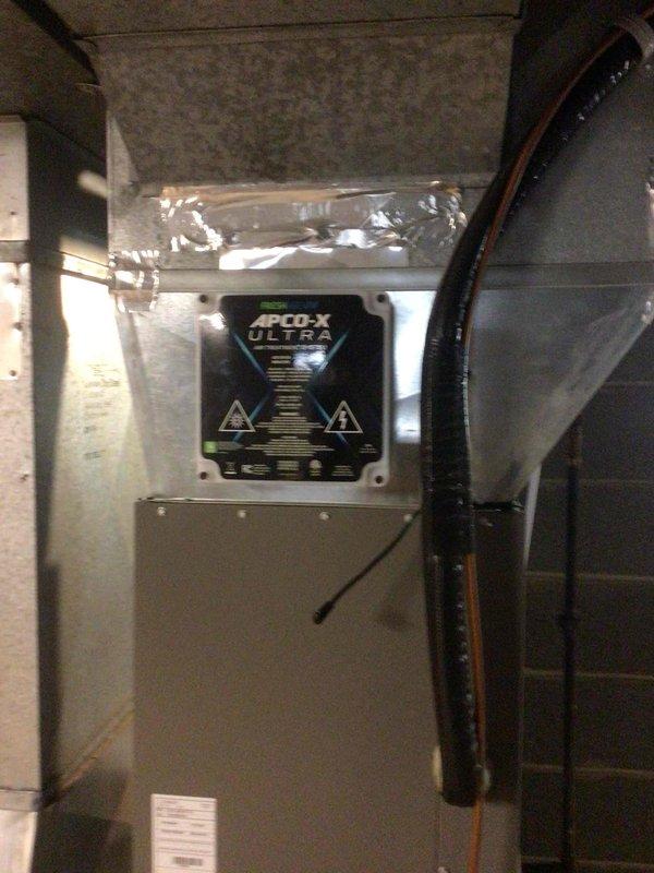 Responded to service call for water leaking from bottom of air handler unit. Upon inspection, found condensate drain line partially clogged, causing water to accumulate in drain pan. Cleared blockage from condensate line and verified complete drainage of pan. Customer reported APCO-X UV light system not functioning. Tested transformer output and found no 24-volt power supply. Replaced defective transformer and confirmed proper voltage restoration. UV light still inoperative after transformer replacement. Removed UV bulb and discovered glass envelope shattered at base. Ordered replacement UV bulb for future installation.