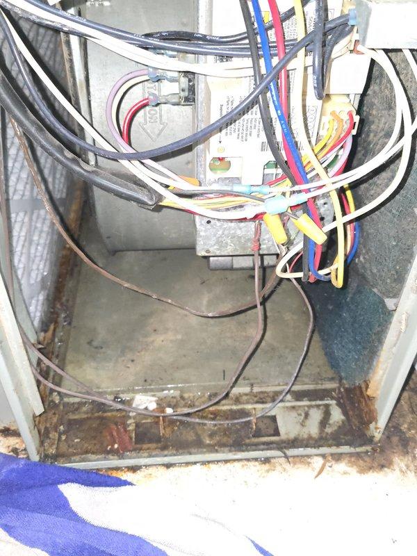 Responded to service call for furnace blower motor not operating and water dripping inside unit. Upon arrival, activated system and confirmed blower motor engaged properly. Connected manifold gauges and identified low refrigerant pressures on 31-year-old R-22 system. Conducted airflow verification and inspected filter, blower wheel, and evaporator coil for obstructions. Found minimal dust accumulation on blower wheel insufficient to cause pressure drop. Observed top half of evaporator coil not sweating, indicating partial freezing condition. Determined system is undercharged on R-22 refrigerant, causing evaporator to ice over and restrict airflow, which led to perceived blower failure. Documented extensive corrosion on unit base plate, electrical connections, and copper refrigerant lines with significant rust and oxidation present throughout equipment. Photographed deteriorated conditions showing moisture damage and age-related wear on metal components and housing. Reviewed findings in