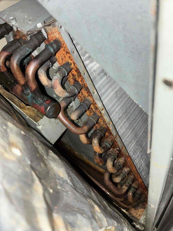 Responded to service call for furnace blower motor not operating and water dripping inside unit. Upon arrival, activated system and confirmed blower motor engaged properly. Connected manifold gauges and identified low refrigerant pressures on 31-year-old R-22 system. Conducted airflow verification and inspected filter, blower wheel, and evaporator coil for obstructions. Found minimal dust accumulation on blower wheel insufficient to cause pressure drop. Observed top half of evaporator coil not sweating, indicating partial freezing condition. Determined system is undercharged on R-22 refrigerant, causing evaporator to ice over and restrict airflow, which led to perceived blower failure. Documented extensive corrosion on unit base plate, electrical connections, and copper refrigerant lines with significant rust and oxidation present throughout equipment. Photographed deteriorated conditions showing moisture damage and age-related wear on metal components and housing. Reviewed findings in