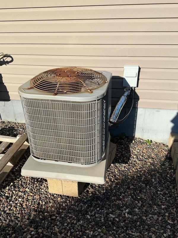 Responded to no-cooling complaint on 13-year-old system where customer reported hissing noise followed by loss of cooling capacity. Upon inspection, connected manifold gauges and found elevated system pressure but inadequate cooling performance. Verified clean air filter and proper airflow with no coil icing present. Tested filter dryer and attempted refrigerant charge adjustment with no improvement in system performance. Performed TXV diagnostic test by exposing sensing bulb to hot water with no change in suction pressure, then immersed bulb in ice water which caused pressure drop, indicating thermostatic expansion valve is closing properly but failing to open correctly. Diagnosis confirmed faulty TXV preventing proper refrigerant metering and system operation. Documented findings with photos of outdoor condensing unit installation. Provided customer with repair options and pricing for TXV replacement. Awaiting customer decision to proceed with recommended repairs.