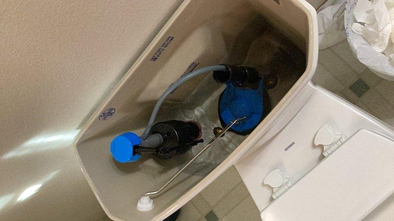 Completed comprehensive plumbing inspection of residential property, including evaluation of outdoor spigot for wear as requested and interior toilet tank components. Documented toilet fill valve assembly with blue float mechanism, flush valve with flapper, and braided supply line connections, noting water staining in tank and moisture damage on surrounding wooden surfaces. All plumbing fixtures were inspected and photographed for maintenance records.