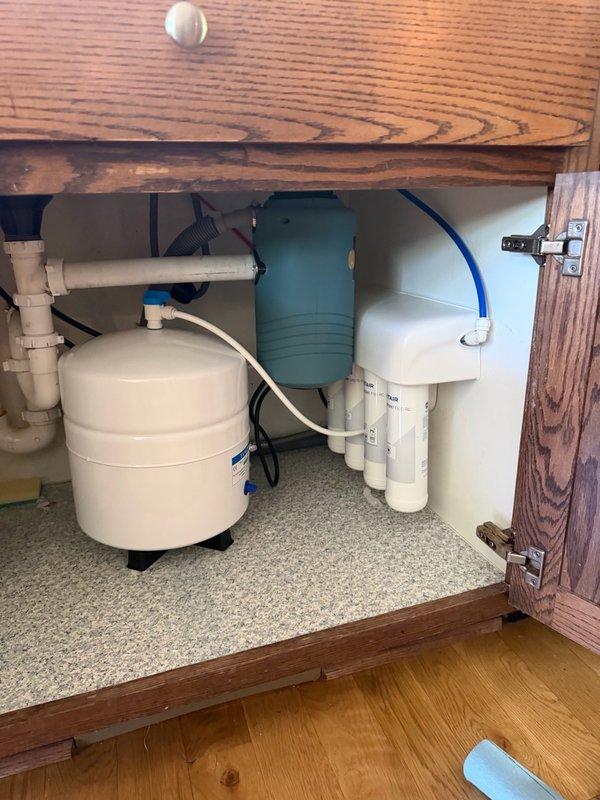 Responded to a water leak located under the kitchen sink originating from a reverse osmosis system. Upon arrival, found active leak from the RO drain line. During diagnostic inspection, discovered the reverse osmosis unit was operating without a flow restrictor, which is a critical component for proper system function and pressure regulation. Installed a complete reverse osmosis system with all required components, including the previously missing flow restrictor. Reconfigured and re-ran the drain line to connect properly to the standpipe for code-compliant drainage. Verified all connections were secure and tested the system for proper operation and absence of leaks. System is now functioning correctly with no active water leakage detected.