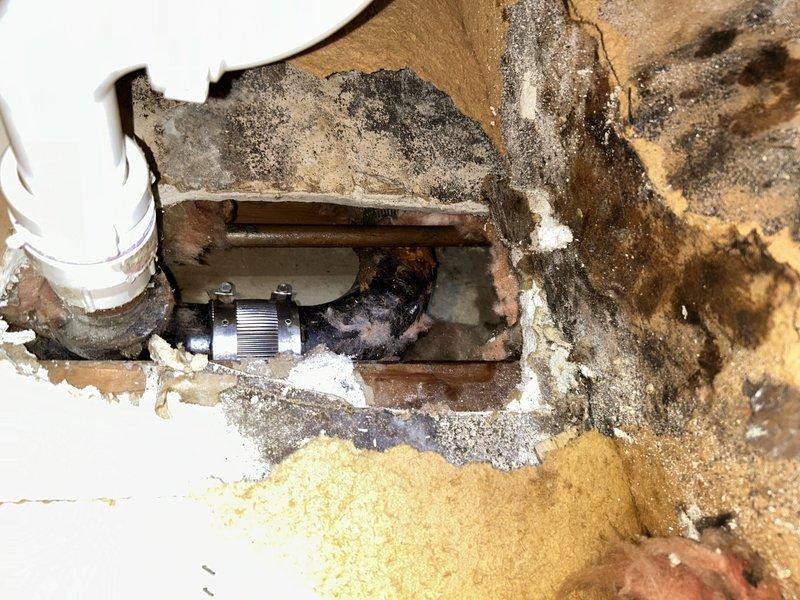 Responded to bathroom sink leak causing water infiltration into parking garage below the unit. Upon investigation, accessed the vanity cabinet and identified a failed mission band coupling behind the wall connecting to the sink drain assembly. Extensive water damage was evident, including deteriorated drywall, mold growth, and debris accumulation within the cabinet interior. Removed damaged section of wall to expose the defective mission band fitting, which showed signs of corrosion and failure at the connection point. Replaced the compromised mission band and associated piping with new components to restore proper drainage function and eliminate the leak source. Documented the extent of water damage and mold contamination present in the wall cavity and surrounding materials for further remediation consideration.