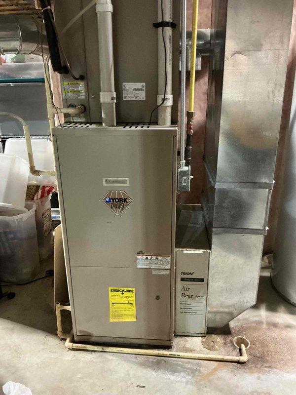 Responded to no cooling complaint on 10+ year old York system where indoor blower motor would not operate. Diagnosed AC unit running briefly before shutting down, causing both outdoor unit and indoor blower to cease operation without tripping low-voltage fuse. Systematically tested components and isolated issue to outdoor unit by disconnecting it from furnace, confirming indoor blower operated normally when separated. Further testing identified faulty crankcase heater causing system shutdown. Disconnected defective crankcase heater from contactor, restoring full system operation. System currently running and cooling properly with crankcase heater isolated. Submitted parts pricing request and recommended system replacement due to age and condition of equipment.