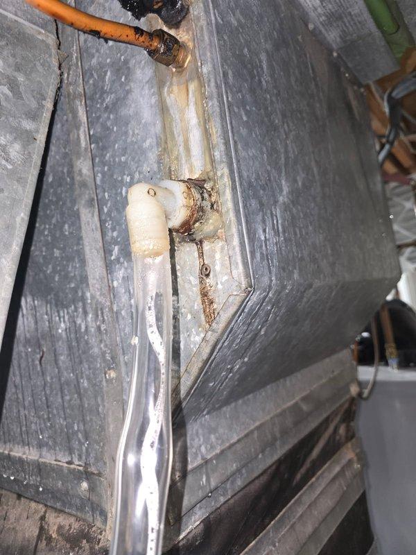 Responded to water leak complaint on Heil R22 air conditioning system. Upon inspection, replaced condensate tube and fitting, but leaking persisted. Further investigation revealed cracked evaporator coil and heavily rusted condensate pan allowing water to leak onto heat exchanger and into drain area. Observed extremely hot liquid line indicating potential refrigerant restriction, dirty outdoor coil, and missing condenser data plate preventing model confirmation. Air filter condition was acceptable. Due to extent of damage including compromised evaporator coil, failed condensate pan, and overall system age, recommended complete system replacement including evaporator coil and condenser unit. Documented conditions with photos showing corroded drainage components and rust staining at pipe connections.