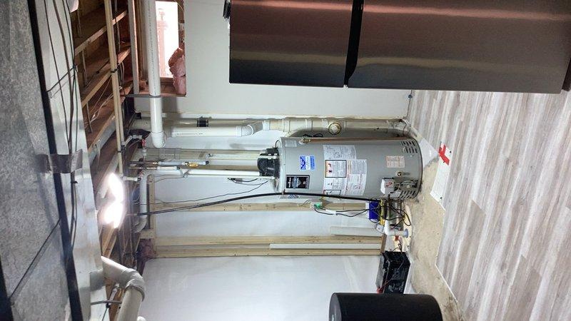 Completed callback service to relocate water heater to its original position following basement waterproofing and drain tile installation. Reconnected all plumbing lines, gas connections, and venting system to the relocated water heater unit. Verified proper operation of all connections and documented final installation with photographs showing completed mechanical room setup with water heater, associated piping, and auxiliary equipment properly positioned and functioning.