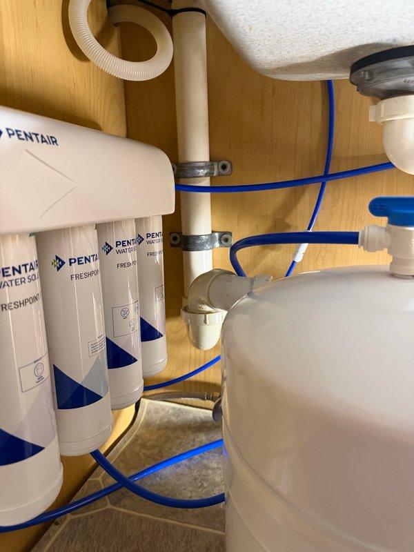 Responded to callback for persistent loud gurgling noise from reverse osmosis system drain line following previous filter replacement service. Rerouted RO drain line to dishwasher standpipe and installed check valve to eliminate noise and prevent backflow. Tested system operation to verify complete resolution of drainage noise issue.