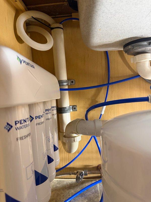 Responded to callback for persistent loud gurgling noise from reverse osmosis system drain line following previous filter replacement service. Rerouted RO drain line to dishwasher standpipe and installed check valve to eliminate noise and prevent backflow. Tested system operation to verify complete resolution of drainage noise issue.