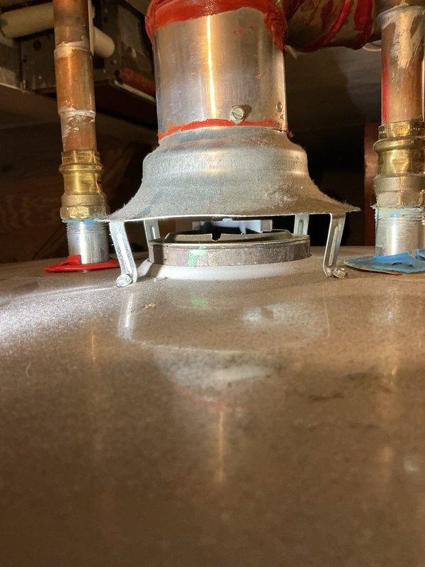 Responded to service call for melting observed on top of 50-gallon natural gas chimney vent water heater. Upon inspection, discovered improper chimney venting installation identified during home inspection. Measured chimney vent and found back pitch of approximately 1 inch over 1-foot span, preventing proper draft. Observed heat damage and melting on trim rings at water heater nipple connections due to inadequate venting. Additionally found flue damper cocked approximately quarter turn out of proper position, further restricting exhaust flow.

Disassembled existing chimney vent system and shortened vertical portion to correct improper pitch. Reinstalled chimney vent piping with proper upward pitch to ensure adequate draft. Adjusted and repositioned flue damper to correct alignment. Fired water heater and verified proper draft by confirming heat rising through vertical chimney portion. Confirmed all exhaust gases venting appropriately with no heat buildup at trim rings or top of unit. S