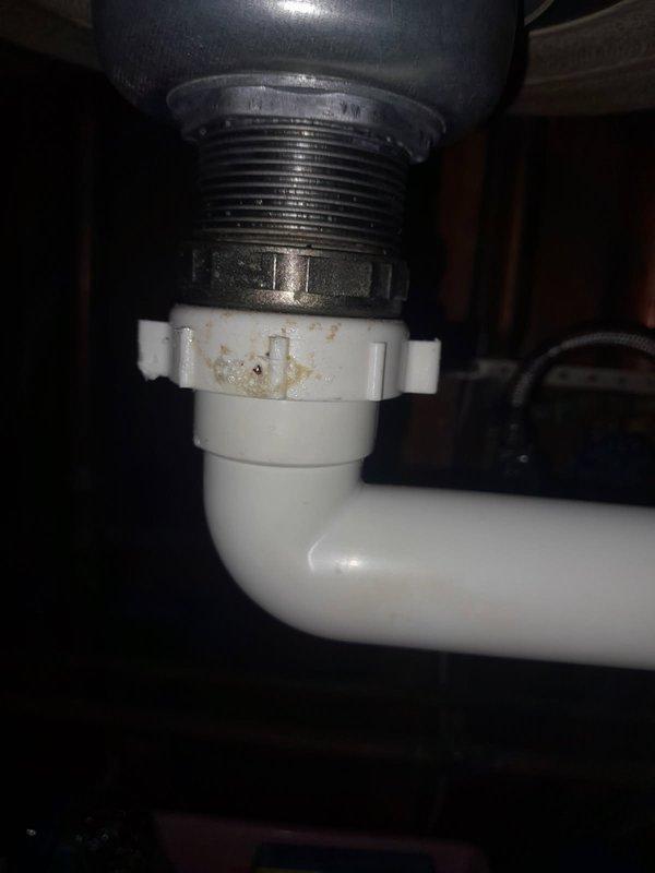 # Kitchen Sink Drain Repair

Responded to a water leak originating from the kitchen sink drain connection. Upon inspection, identified a cracked plastic coupling nut at the tailpiece connection point, which was causing water to seep during drainage. The deteriorated nut showed visible signs of stress fractures and mineral buildup, compromising the seal integrity of the P-trap assembly.

Removed the failed coupling nut and replaced it with a new white PVC slip joint nut, ensuring proper threading and hand-tightening to manufacturer specifications. Verified all connections within the P-trap assembly were secure and tested the repair by running water through the drain system to confirm leak elimination and proper drainage flow.