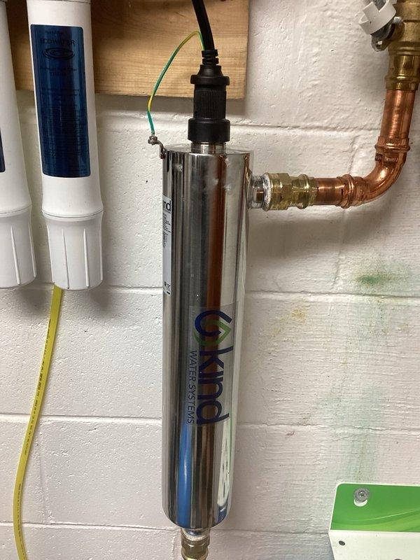 Performed water treatment system maintenance including UV bulb and filter service. Installed customer-supplied UV bulb into existing chrome cylindrical UV filtration unit mounted on wall alongside white filter housing with blue cartridge. Submitted parts request for additional filters per customer's request for future replacement.