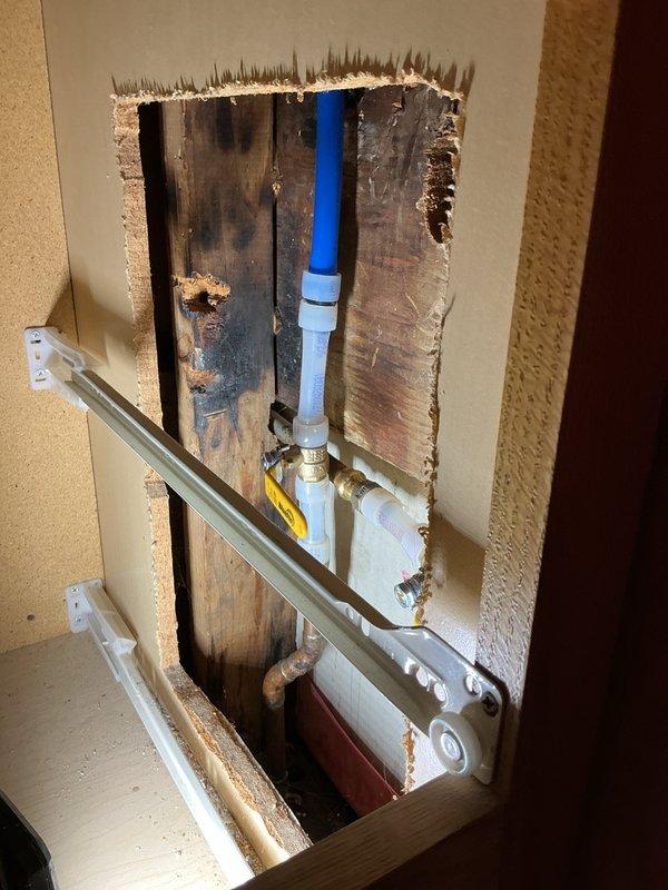 Responded to a water leak behind shower originating from cold water supply line. This location had previously experienced a hot water leak that was repaired approximately one year ago. Accessed the plumbing system through ceiling and wall openings to locate and assess the leak source. Identified failed section of cold water piping requiring replacement. Removed compromised piping section and installed new piping with appropriate fittings and connections using PEX and brass connectors. Verified all connections were secure and tested system for proper operation and absence of leaks. Evidence of previous moisture exposure was visible on surrounding wooden framing from prior leak incident.