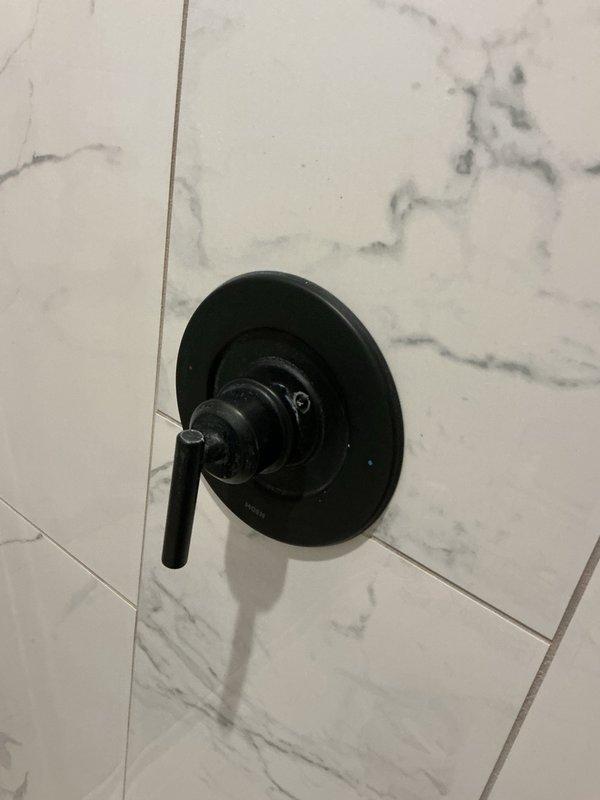 Responded to reported water leak in master shower dripping into basement mechanical room. Upon arrival, area had been dried and no active leak was visible. Conducted diagnostic testing by running shower for 20 minutes to attempt replication of leak condition. No dripping or moisture detected during test period. Removed escutcheon plate and shower valve handle to inspect behind wall assembly. All components and surrounding areas were completely dry with no evidence of moisture intrusion or valve failure. Based on findings and information provided, determined likely cause was water dripping from washcloth that had been hanging on shower rack near valve, creating appearance of plumbing leak. Reassembled shower valve components. Advised to monitor after each shower use and contact if leak recurs.