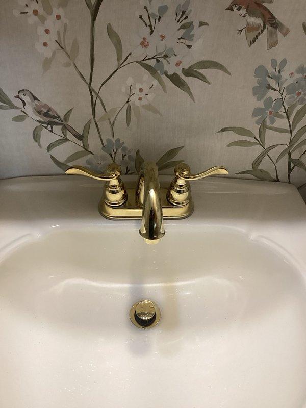 Installed customer-supplied bathroom vanity faucet with polished brass finish and matching drain assembly on white porcelain sink. Completed installation of two-handle traditional style faucet with curved spout, ensuring proper connections and testing for leaks. Installation did not include hole drilling, supply lines, or shut-off valve replacement, with customer advised that no warranty applies to customer-supplied materials.