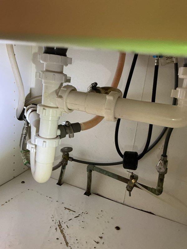 Responded to water leak under kitchen sink occurring intermittently without sink or dishwasher use. Upon inspection, identified backed-up drain line causing water to overflow from P-trap assembly when water softener discharged. Confirmed drain blockage was preventing proper drainage of softener discharge water, resulting in backup through sink drain system. Documented plumbing configuration including white PVC P-trap assembly, supply lines, and connections. Scheduled drain technician for follow-up service to clear obstruction and restore proper drainage function.