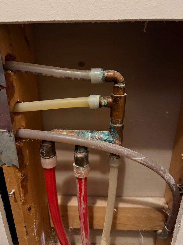 Responded to report of toilet leak affecting lower level. Upon investigation, determined leak was not originating from toilet fixture but from a hot water line manifold located in the wall cavity behind the toilet. Opened wall to access plumbing assembly and identified corroded copper fittings and compromised pipe connections showing signs of oxidation and verdigris formation. Replaced damaged section of hot water piping and defective fittings with new materials. Secured all connections and tested system for proper operation and leak elimination. Restored wall access opening upon completion of repairs.