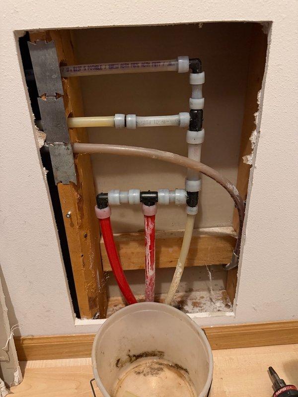 Responded to report of toilet leak affecting lower level. Upon investigation, determined leak was not originating from toilet fixture but from a hot water line manifold located in the wall cavity behind the toilet. Opened wall to access plumbing assembly and identified corroded copper fittings and compromised pipe connections showing signs of oxidation and verdigris formation. Replaced damaged section of hot water piping and defective fittings with new materials. Secured all connections and tested system for proper operation and leak elimination. Restored wall access opening upon completion of repairs.