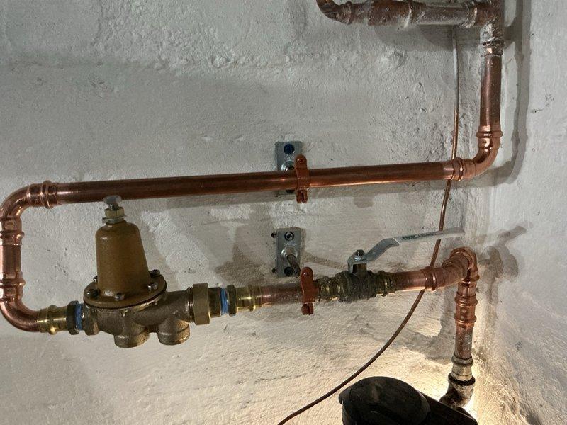 Responded to excessive water pressure issue measuring 110 psi at the main water supply line. Installed a three-quarter inch brass pressure reducing valve with isolation valves on the incoming copper water line to protect plumbing fixtures and appliances from potential damage. Mounted the PRV assembly to the basement wall using proper support brackets and configured the regulator to deliver a safe operating pressure of 70 psi. Tested system operation and verified consistent pressure output at the reduced setting.