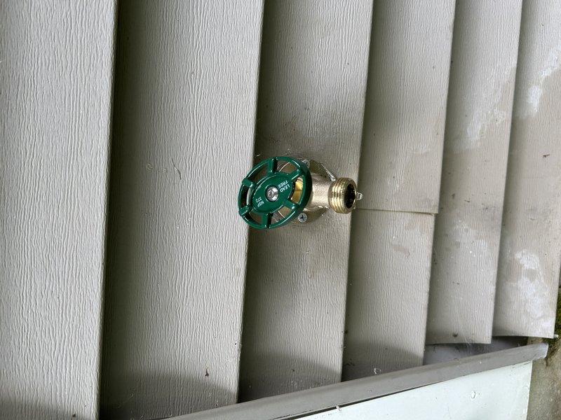 Replaced two exterior hose bibs that were leaking with new brass valve assemblies featuring green wheel handles, mounted on vinyl siding. Inspected basement plumbing connections including copper supply lines, ball valves, and manifold assembly to verify proper operation and ensure no additional leaks were present in the system.