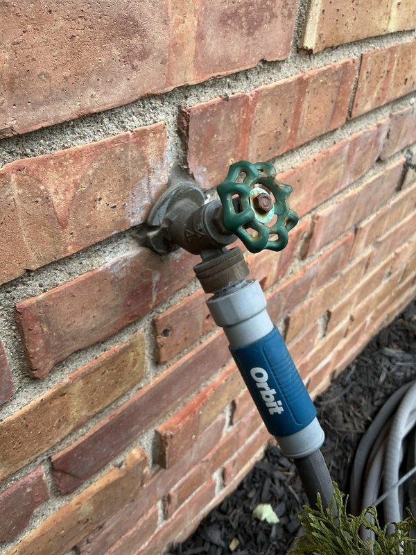 Responded to exterior water leak at outdoor hose bib mounted on brick wall. Upon arrival, found garden hose fused to the spigot's vacuum breaker assembly, preventing proper removal and causing significant water leakage. Water supply had been shut off prior to arrival. Successfully removed the compromised hose from the threaded connection and vacuum breaker. Inspected the brass spigot assembly with wheel-style valve handle for additional damage and assessed the condition of the fixture, noting weathering and oxidation consistent with age and outdoor exposure. Provided replacement options and cost estimates for the vacuum breaker assembly and potential full spigot replacement to prevent future leakage issues.