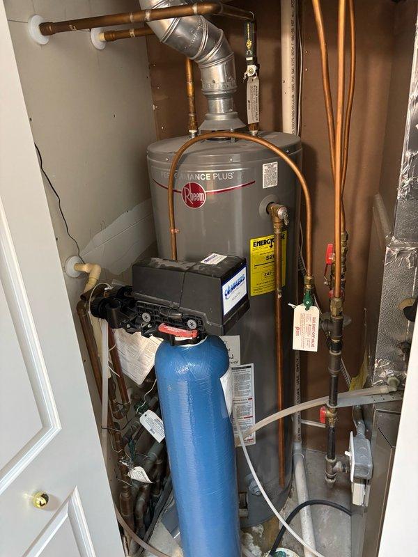 Responded to no hot water complaint at residential property. Upon inspection, found Rheem gas water heater in non-operational state with pilot light extinguished. Identified active water leak originating from behind the unit with visible water stream and saturated insulation near the burner assembly. Successfully relit pilot light to restore temporary hot water function while property owner evaluates replacement options. Documented equipment condition with photographs showing water heater installation alongside water softener system in utility closet. Advised that leak indicates tank failure and unit requires replacement in near future.