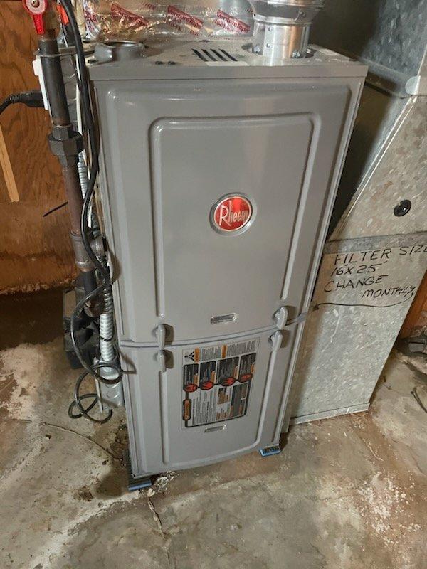 Responded to no cooling complaint with water leaking on floor. Found tripped outlet supplying power to condensate pump, causing system shutdown and water overflow onto concrete floor. Reset circuit breaker and restored power to pump, which resumed normal condensation removal operation. Inspected unit and noted rust staining and water streaks on equipment and surrounding area from previous overflow. Verified Rheem furnace returned to normal operation, checked air filters, and confirmed condensate drain system functioning properly with pump actively removing water from drain pan.