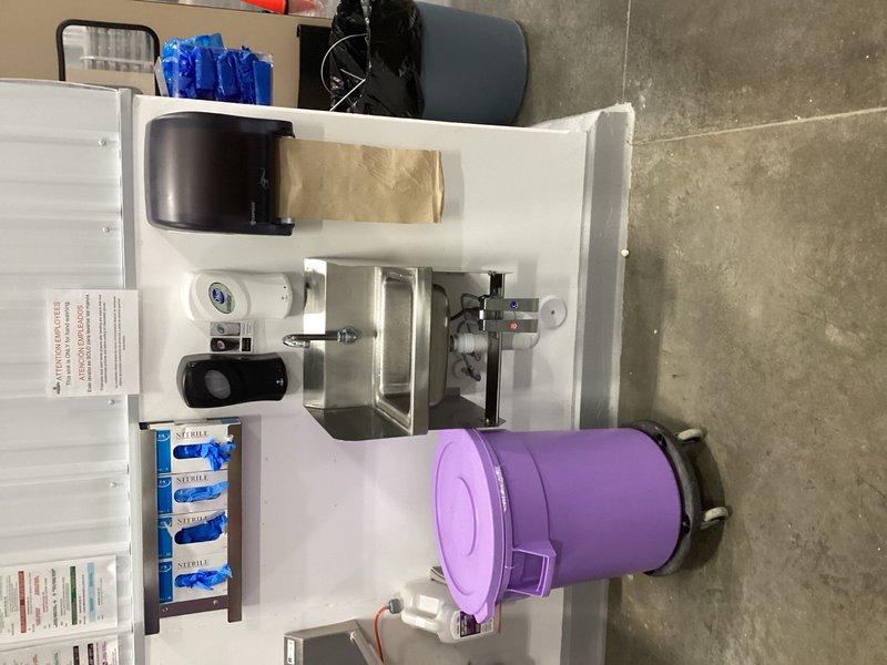 Completed comprehensive plumbing inspection of commercial facility including water heater relocation, PRV pressure verification, vacuum breaker testing, mixing valve functionality checks, water heater flushing and maintenance, faucet temperature and component testing, and eyewash station evaluation. Identified multiple deficiencies requiring attention: mixing valve in unisex bathroom requires adjustment, mixing valve and foot pedal at main handwashing sink need replacement, dishwashing room handwashing sink drain experiencing backup issues, and cold cartridge in lab handwashing sink requires replacement. Documented system conditions with photographs showing aged copper piping with heavy oxidation and pressure gauge monitoring, as well as portable handwashing station setup. Estimate to be prepared for identified repairs and component replacements.