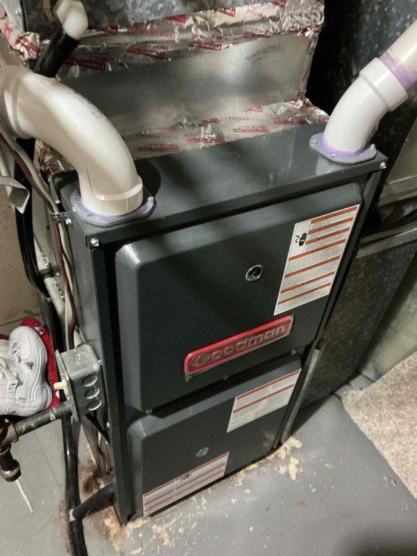 Responded to a no-cooling complaint on a 26-year-old Goodman air conditioning system. Upon arrival, found the outdoor unit operational but compressor drawing near maximum amperage, resulting in excessive high-side pressure and temperature that prevented adequate cooling capacity. Performed comprehensive system diagnostics including electrical component testing, airflow verification, and heat exchange inspection. Confirmed contactor operation within specifications, capacitor testing normal, condenser coil relatively clean with acceptable airflow, indoor air filter clean, evaporator coil free of restrictions, and blower motor set to proper cooling speed. High-side pressure and temperature readings confirmed compressor inefficiency as primary failure point. All safety controls functioning properly with no immediate hazards identified. Documented findings with photographic evidence of indoor furnace/air handler installation and outdoor condensing unit condition. Reviewed repair versus repl