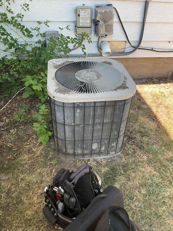 Responded to a no-cooling complaint on a 26-year-old Goodman air conditioning system. Upon arrival, found the outdoor unit operational but compressor drawing near maximum amperage, resulting in excessive high-side pressure and temperature that prevented adequate cooling capacity. Performed comprehensive system diagnostics including electrical component testing, airflow verification, and heat exchange inspection. Confirmed contactor operation within specifications, capacitor testing normal, condenser coil relatively clean with acceptable airflow, indoor air filter clean, evaporator coil free of restrictions, and blower motor set to proper cooling speed. High-side pressure and temperature readings confirmed compressor inefficiency as primary failure point. All safety controls functioning properly with no immediate hazards identified. Documented findings with photographic evidence of indoor furnace/air handler installation and outdoor condensing unit condition. Reviewed repair versus repl