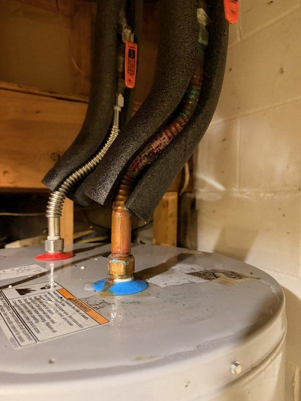 Responded to water heater leak originating from top connections. Upon inspection, identified pinhole leak in flexible copper supply line and additional leak at tee fitting on main water line. Replaced failed flexible water heater supply line with new connector and installed new tee fitting on main water line to eliminate both leak sources. System tested and verified operational with no active leaks upon completion.