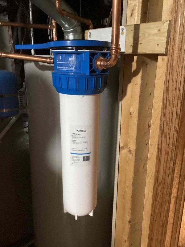 Completed scheduled filter replacement on VIQUA water treatment system installed in basement utility area. Removed existing filter cartridge from housing, installed new replacement filter, and verified proper seating within blue cap assembly and secure connections to copper supply lines. System tested and confirmed operational upon completion.