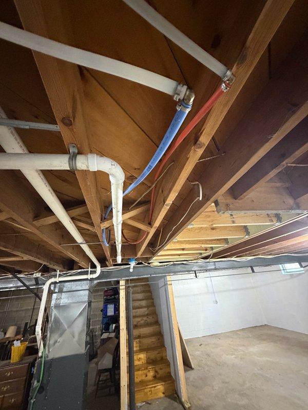 Provided estimate for relocation of electric water heater approximately 2 feet to accommodate new wall construction in basement. Assessment included evaluation of existing water supply piping for potential upsizing to address water pressure concerns, removal of conflicting HVAC ductwork, and installation of new ventilation system. Documented current plumbing configuration and overhead utility routing in unfinished basement area to determine scope of work required for water heater relocation and associated piping modifications.