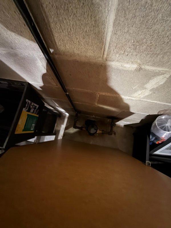 Provided estimate for relocation of electric water heater approximately 2 feet to accommodate new wall construction in basement. Assessment included evaluation of existing water supply piping for potential upsizing to address water pressure concerns, removal of conflicting HVAC ductwork, and installation of new ventilation system. Documented current plumbing configuration and overhead utility routing in unfinished basement area to determine scope of work required for water heater relocation and associated piping modifications.