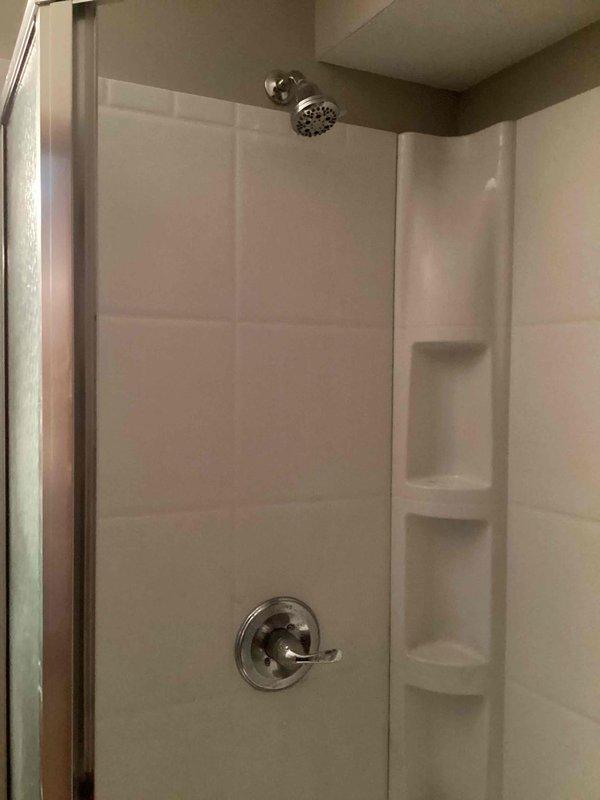 Responded to a continuous dripping shower issue caused by a failed cartridge. Replaced the defective cartridge and installed a complete Moen L2352 chrome shower valve and trim kit, including shower control with single-lever operation, arm, head, and spout. The new system features Scald-Guard temperature protection and water-efficient design, providing reliable temperature and volume control for the residential bathroom shower stall with white textured wall panels and integrated storage niches.