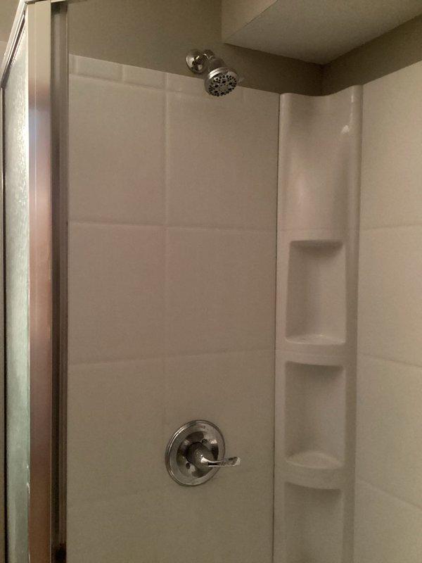 Responded to a continuous dripping shower issue caused by a failed cartridge. Replaced the defective cartridge and installed a complete Moen L2352 chrome shower valve and trim kit, including shower control with single-lever operation, arm, head, and spout. The new system features Scald-Guard temperature protection and water-efficient design, providing reliable temperature and volume control for the residential bathroom shower stall with white textured wall panels and integrated storage niches.