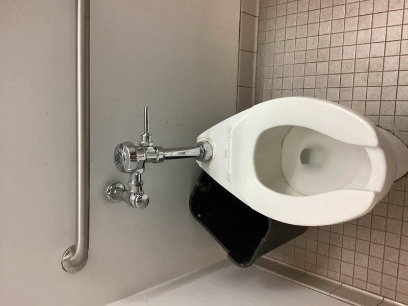 Responded to emergency call for flooding in showroom caused by wall-mounted toilet fixture. Upon inspection, identified active leak at flush valve assembly with water dripping from mounting nut. Tightened flush valve nut to stop leak that had been creating puddle on floor throughout the weekend. Verified proper operation of flush mechanism and checked for additional leaks. Photographed completed repair and documented previously installed flush valve assembly from prior service visit.