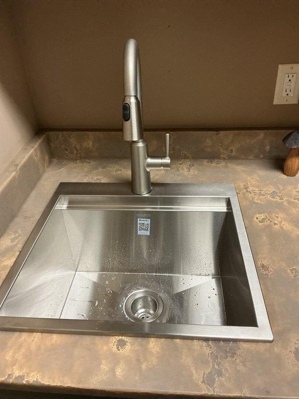 Installed customer-supplied undermount stainless steel sink basin with brushed nickel pull-down faucet and complete drain assembly. Connected hot and cold water supply lines with braided flexible hoses to angle stop valves, installed chrome P-trap configuration with proper venting, and verified all connections for leaks and proper operation.