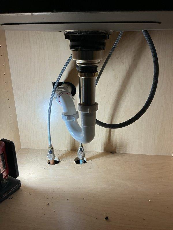 Installed customer-supplied undermount stainless steel sink basin with brushed nickel pull-down faucet and complete drain assembly. Connected hot and cold water supply lines with braided flexible hoses to angle stop valves, installed chrome P-trap configuration with proper venting, and verified all connections for leaks and proper operation.
