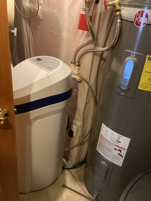 Responded to service call for non-cycling water softener unit. Upon inspection, determined the 16+ year old water softener had failed and was no longer operational. Documented existing installation showing white cylindrical softener unit with control panel connected to water heater via braided stainless steel supply lines with brass fittings and shut-off valve. Recommended complete water softener replacement due to age and system failure, and coordinated with service advisor for equipment replacement and installation scheduling.
