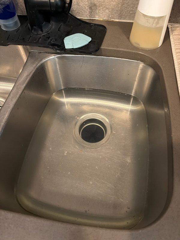 Responded to clogged kitchen sink on disposal side of double-basin sink where water was not draining and garbage disposal was inoperative. Disassembled and cleared the P-trap assembly beneath the garbage disposal, removing accumulated debris causing the blockage. Reassembled drain components, tested system for proper drainage and verified garbage disposal operation restored to normal function.